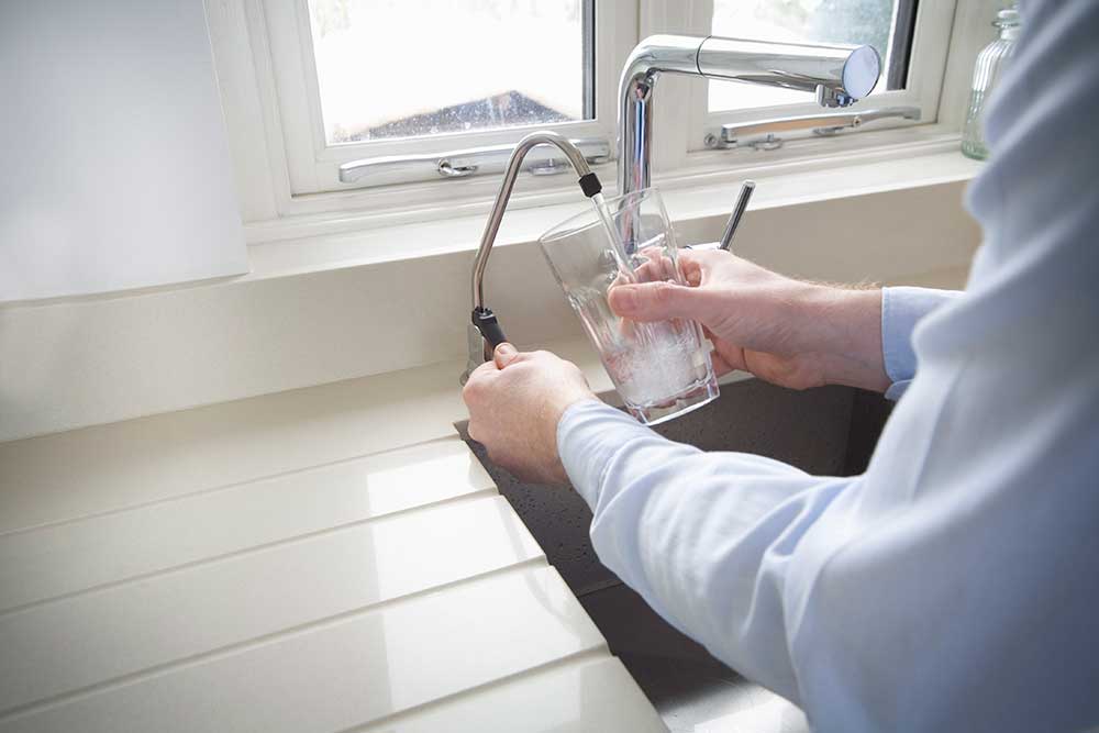 person filling water glass at sink